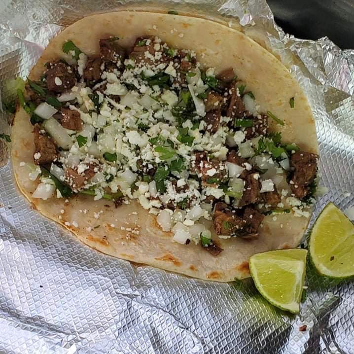 Apartments in Northwest Houston North Eldridge & West Road A Cool Arrow Taco filled with diced meat, onions, cilantro, and crumbled cheese on a foil wrap, with two lime wedges on the side.