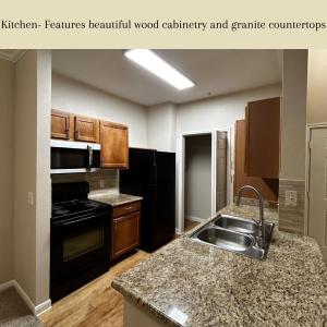 Apartments in Northwest Houston North Eldridge  West Road Kitchen with wood cabinetry, granite countertops, black appliances including a refrigerator, stove, and microwave, double sink, and wood flooring. Text at the top describes the kitchen features.